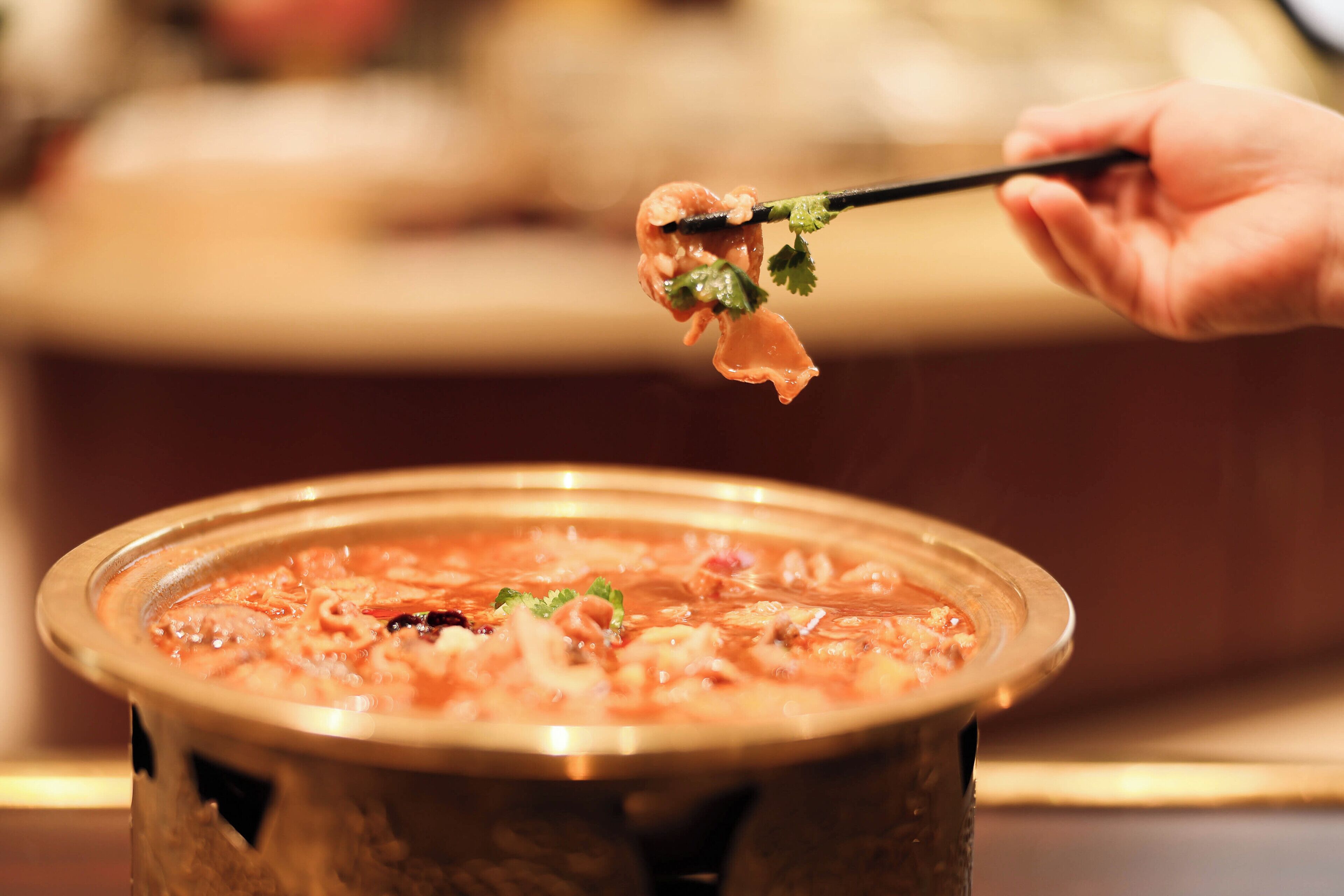 Una mano sosteniendo palillos con comida sobre una olla caliente.