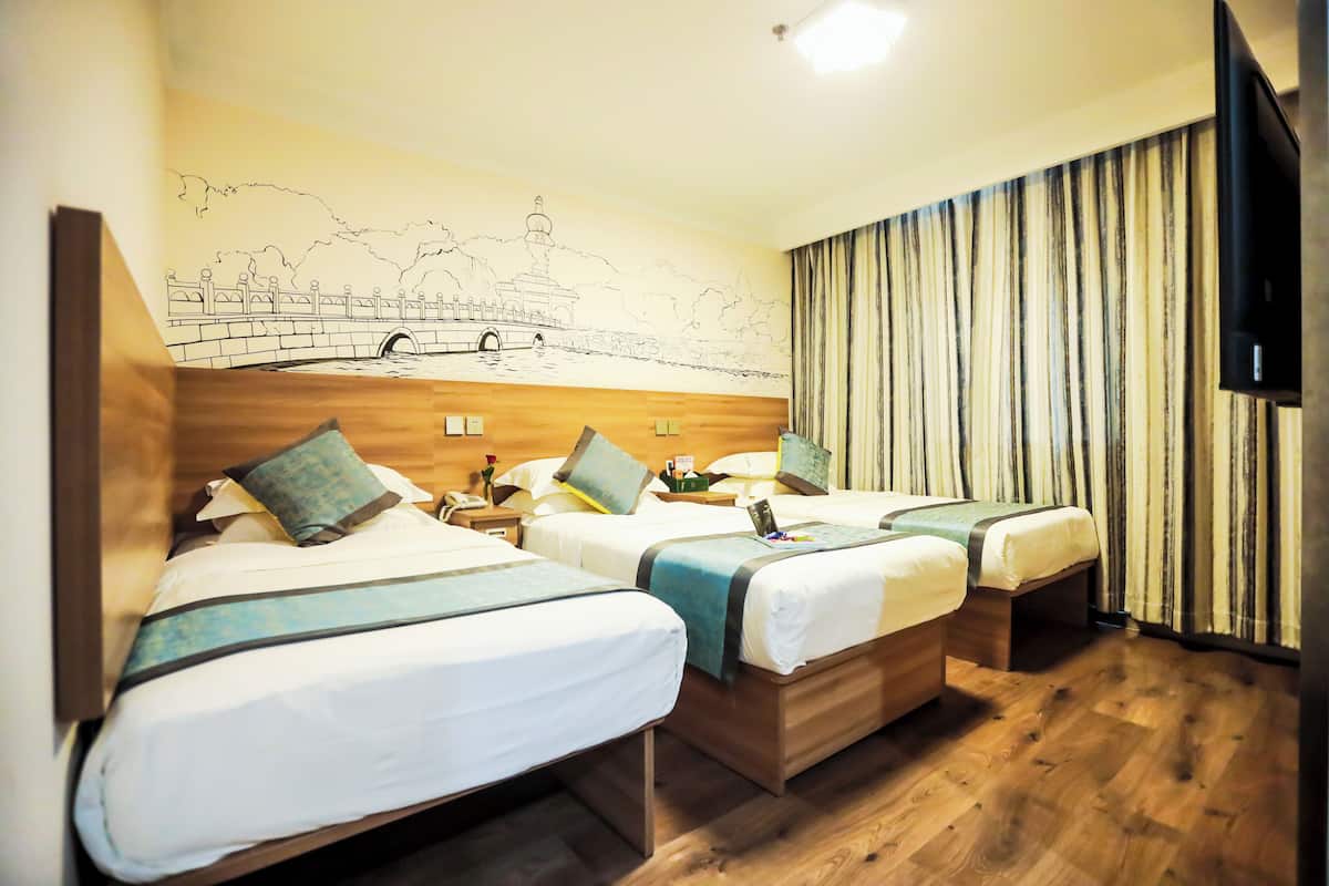 Habitación de hotel con tres camas, cabeceros de madera, un mural de un puente y un televisor a la derecha.