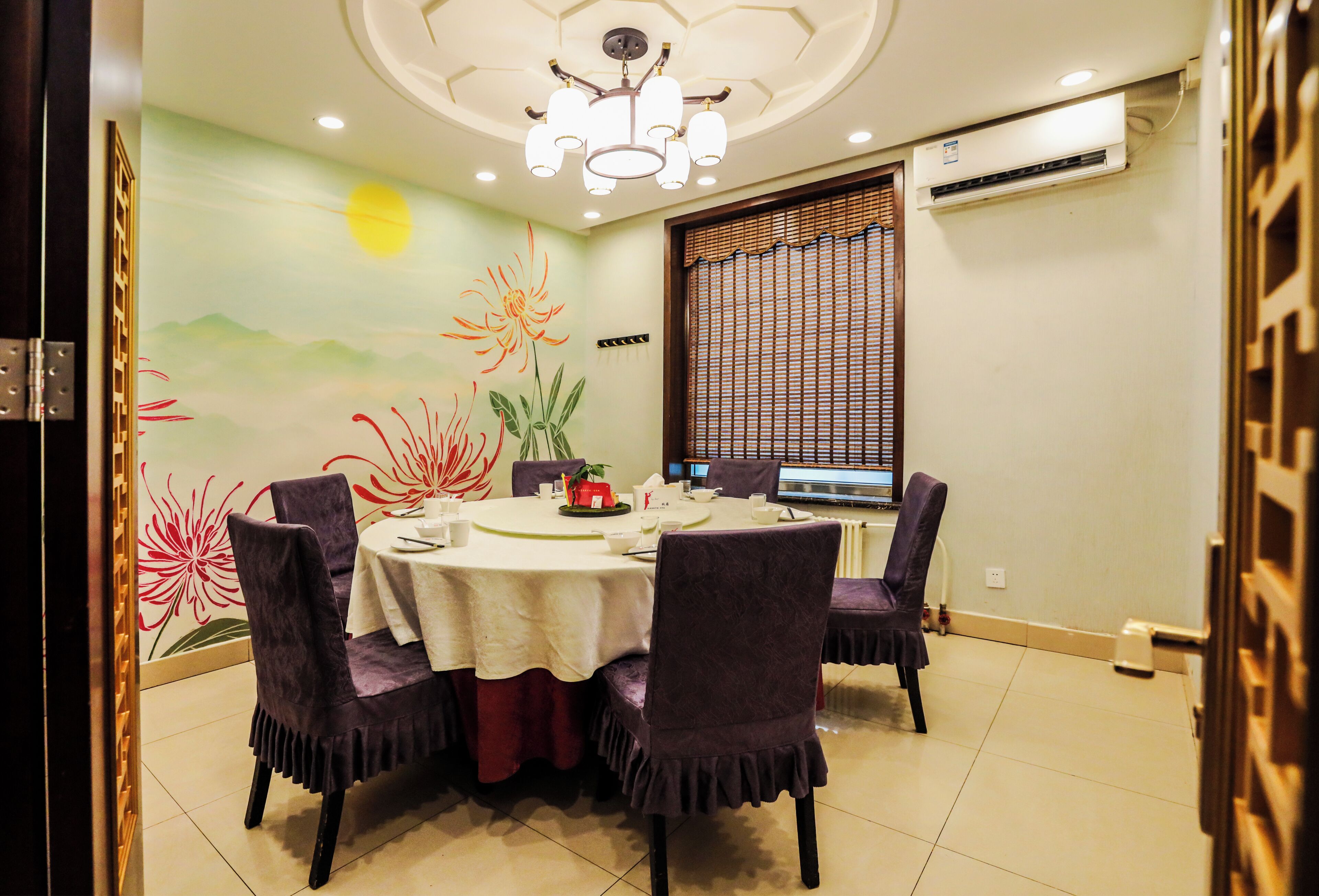 Un espace repas avec une table ronde, des chaises violettes, un lustre et une fresque murale.