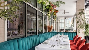 A restaurant with teal upholstered booths and red chairs, white tablecloths, and hanging floral arrangements.