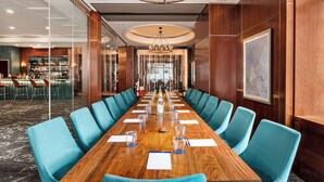 A conference room with a long wooden table, blue chairs, and a chandelier.