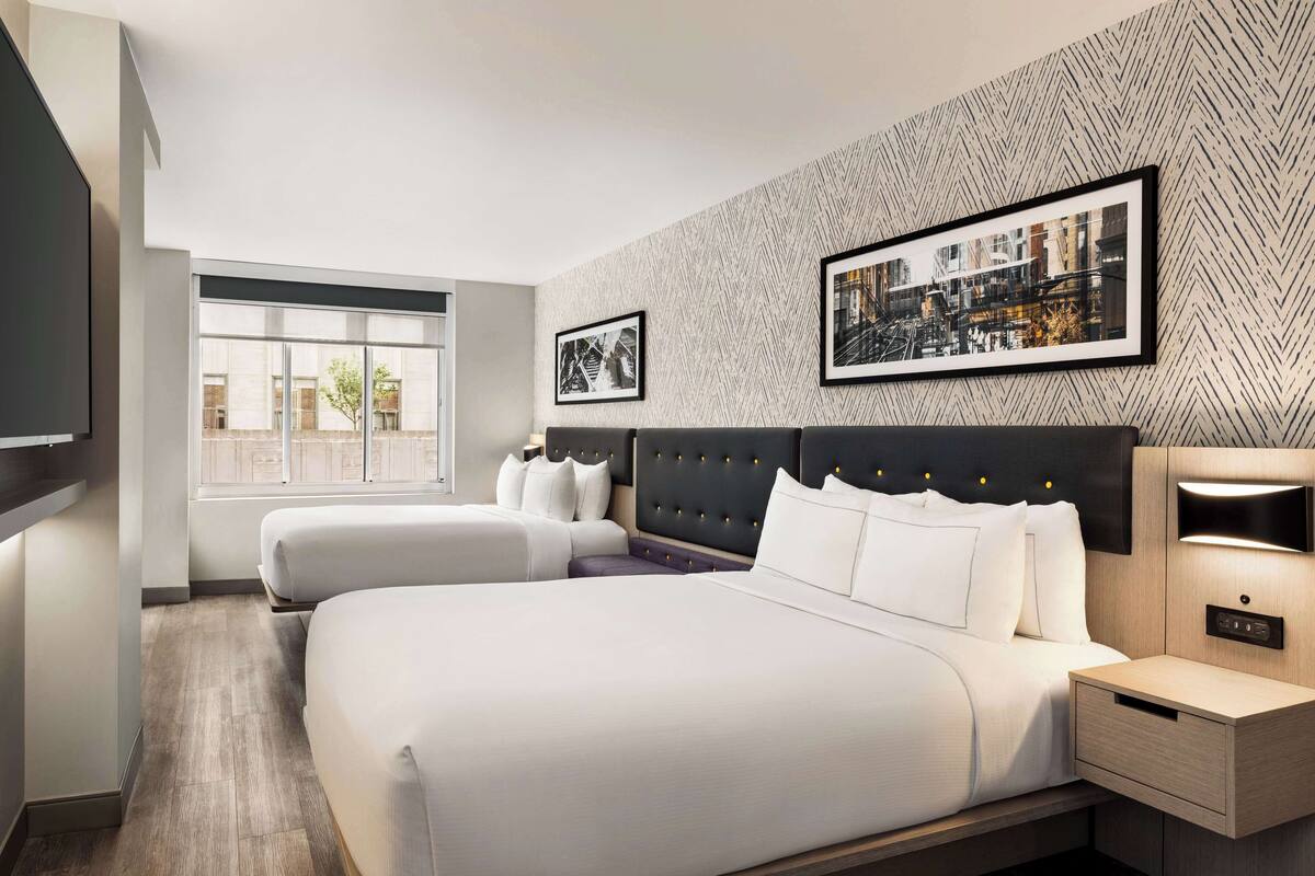 A modern hotel room with a large bed, two smaller beds, a flat-screen TV, a wall-mounted light, and framed pictures.