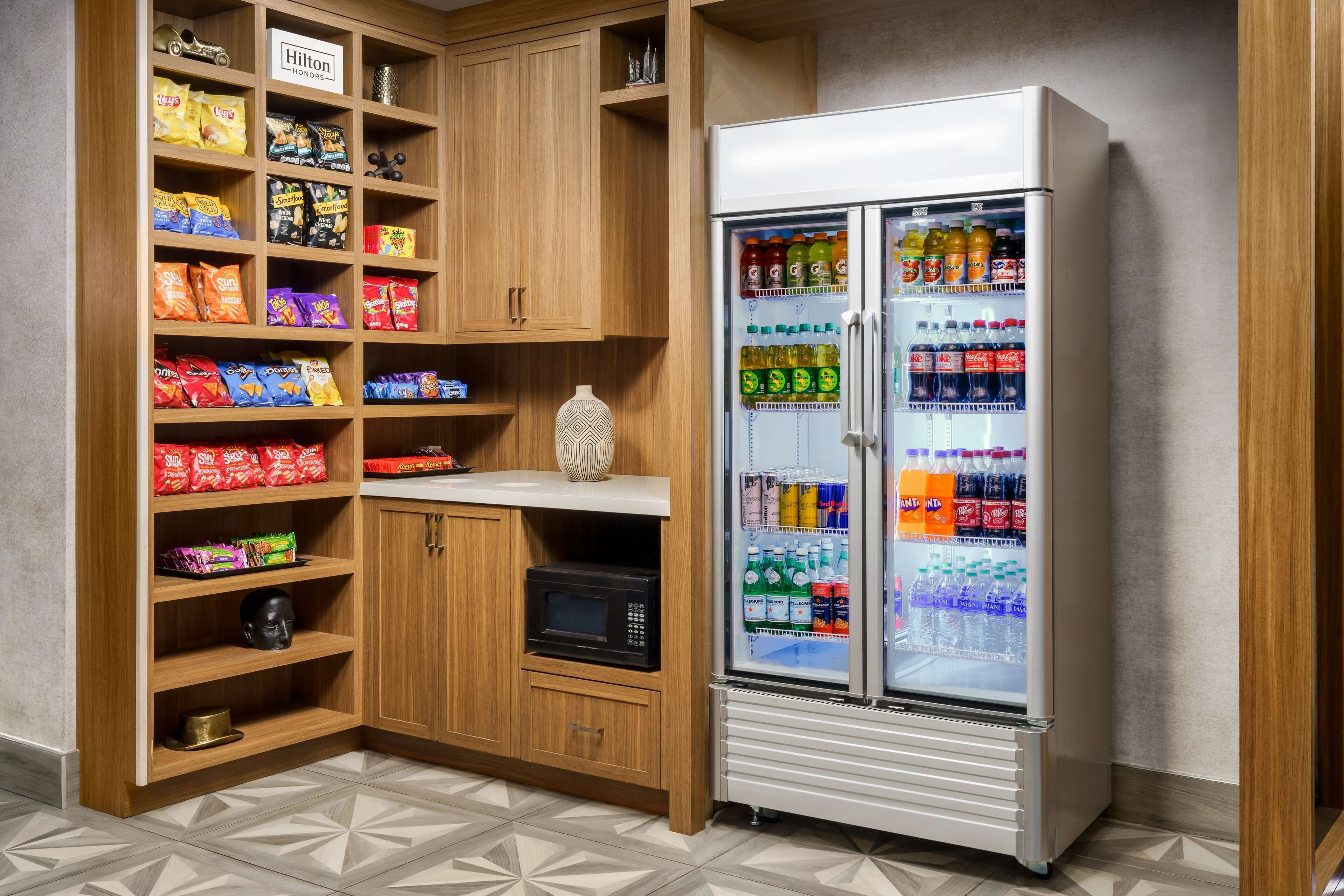 Una kitchenette equipada con microondas, un refrigerador lleno de bebidas y estantes con aperitivos.
