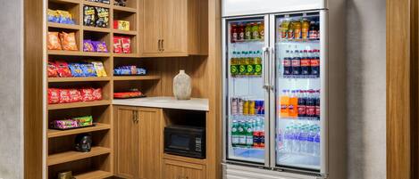 Una kitchenette equipada con microondas, un refrigerador lleno de bebidas y estantes con aperitivos.
