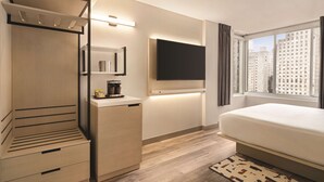 A modern hotel room with a bed, a wardrobe, a flat-screen TV, and a window with a city view.
