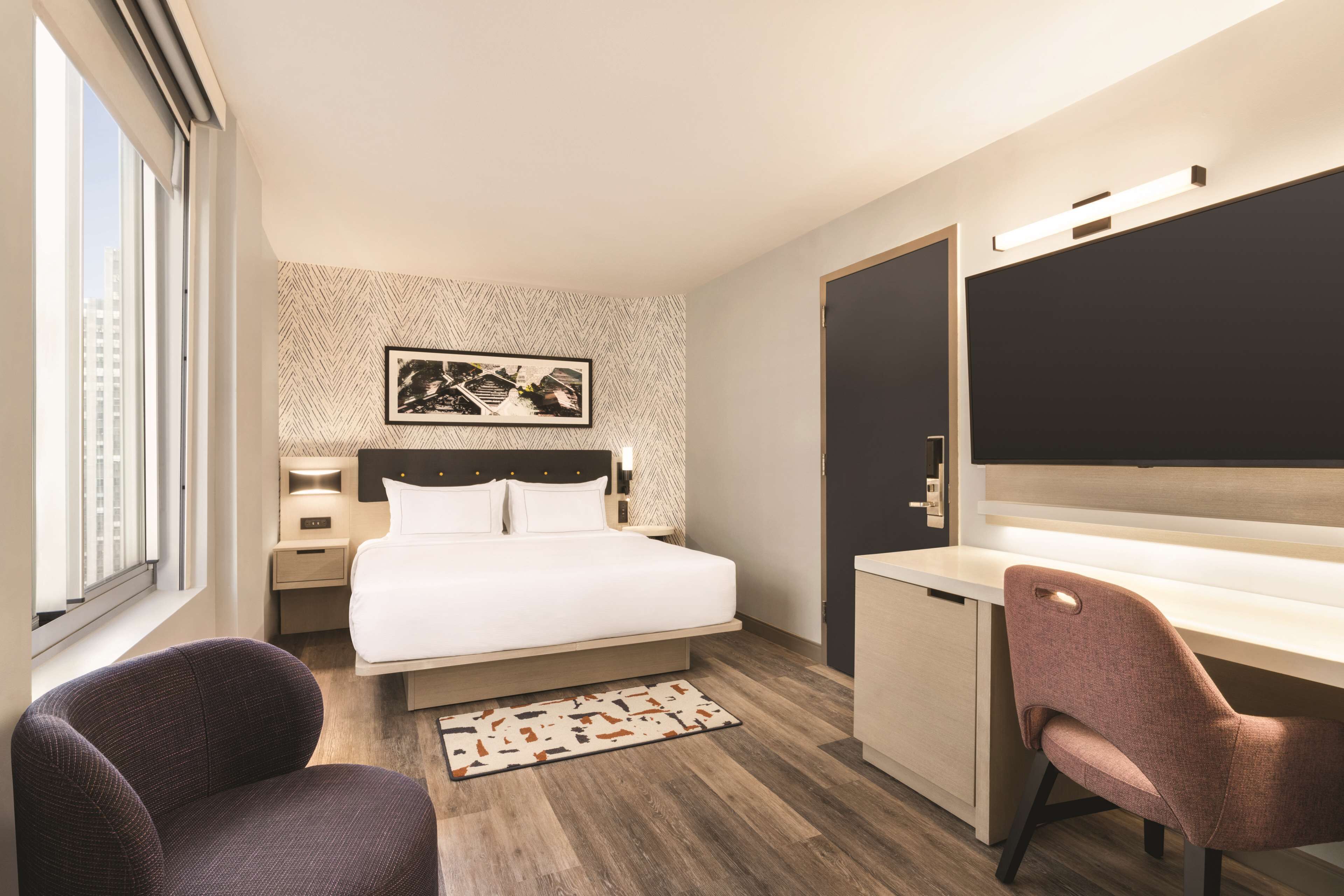A modern hotel room with a bed, desk, and two chairs.