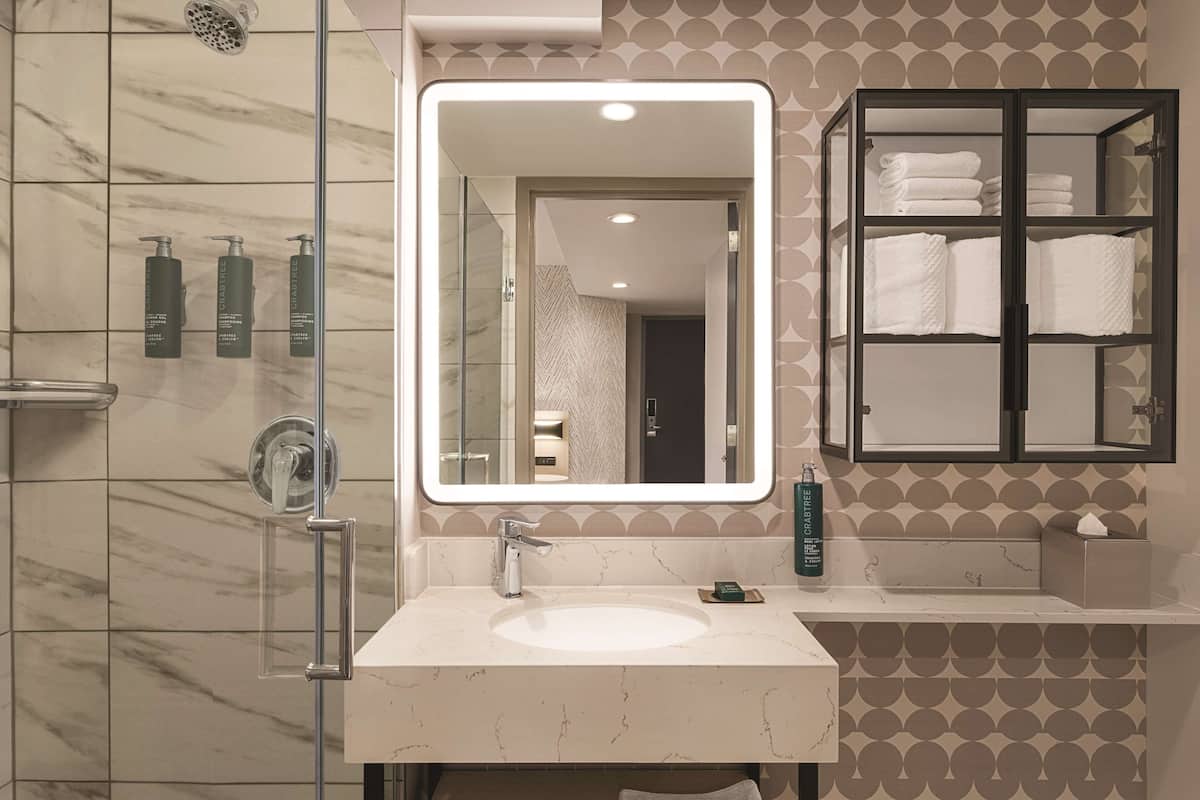 A bathroom with a marble sink, a large mirror, a glass shower enclosure, and a towel rack with folded towels.