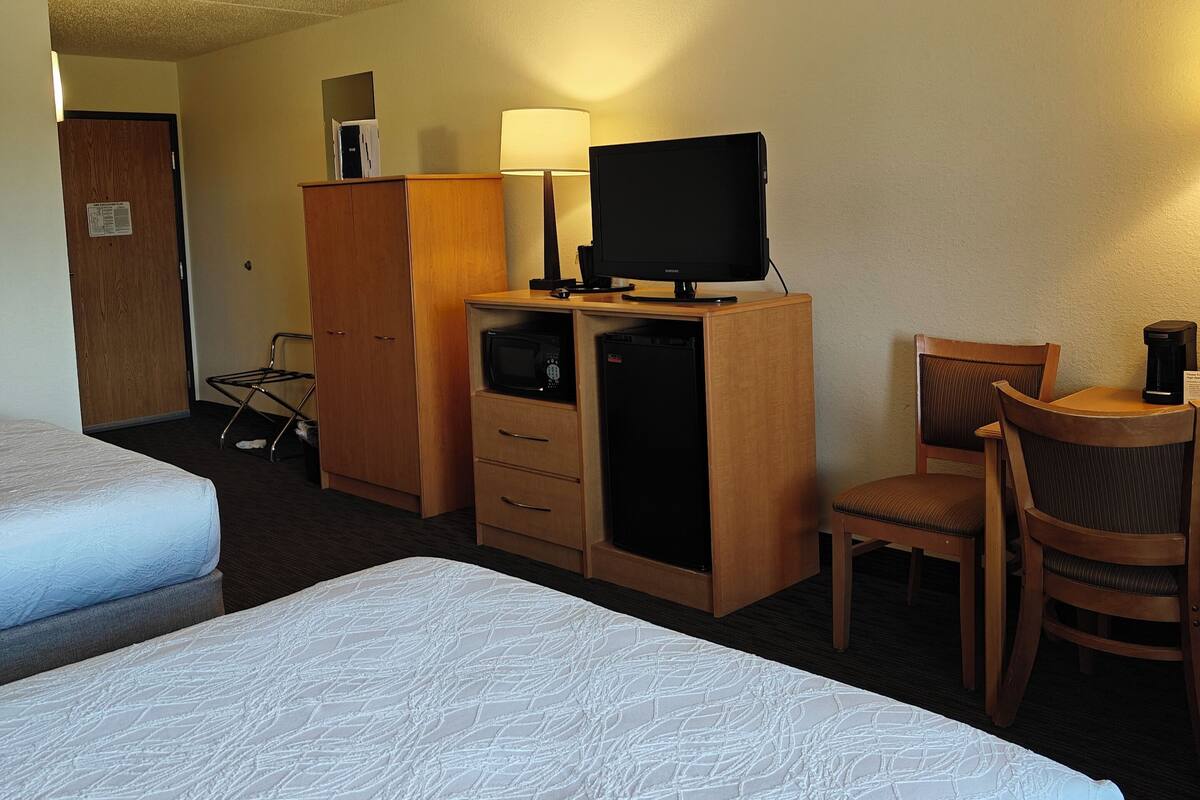 Une chambre d’hôtel avec deux lits, un bureau équipé d’un ordinateur, une lampe, un four à micro-ondes et un réfrigérateur.