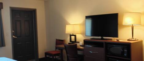Habitación de hotel con dos camas, un escritorio con silla, televisor, lámpara y microondas.