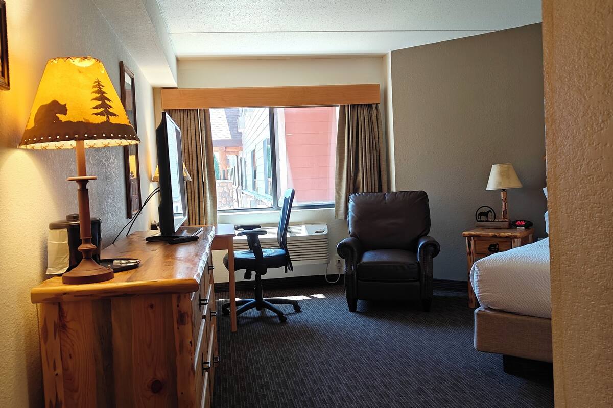 Une chambre d’hôtel équipée d’un bureau, d’une chaise, d’un lit et d’une fenêtre avec des rideaux.