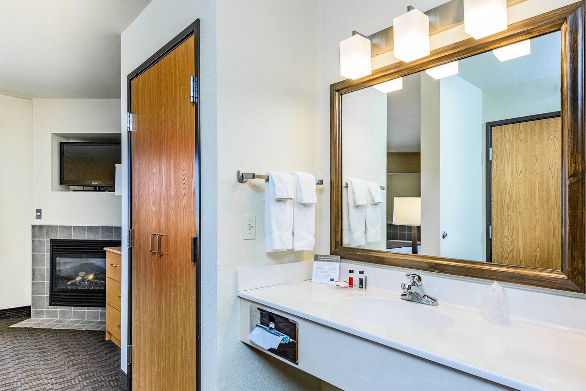 Un baño de hotel con un espejo grande, un lavamanos blanco y una chimenea.