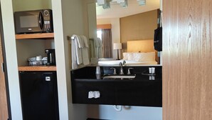 Une chambre d’hôtel compacte comprenant un coin cuisine, un lit, un miroir et une petite poubelle.