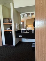 Habitación de hotel compacta con kitchenette, una cama, un espejo y un basurero pequeño.