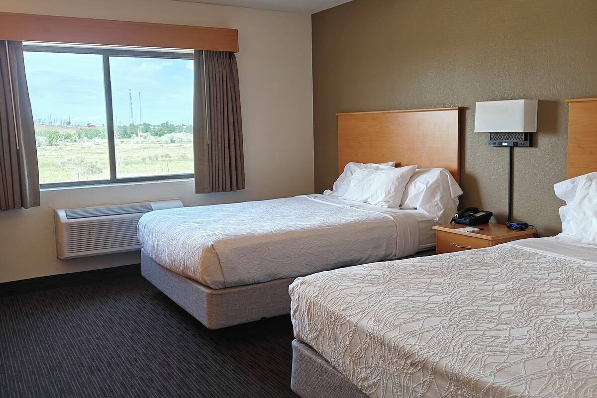 Habitación de hotel con dos camas, un ventanal grande, un ventilador de techo y una mesita de noche con lámpara.