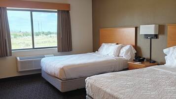 A hotel room with two beds, a large window, a ceiling fan, and a bedside table with a lamp.