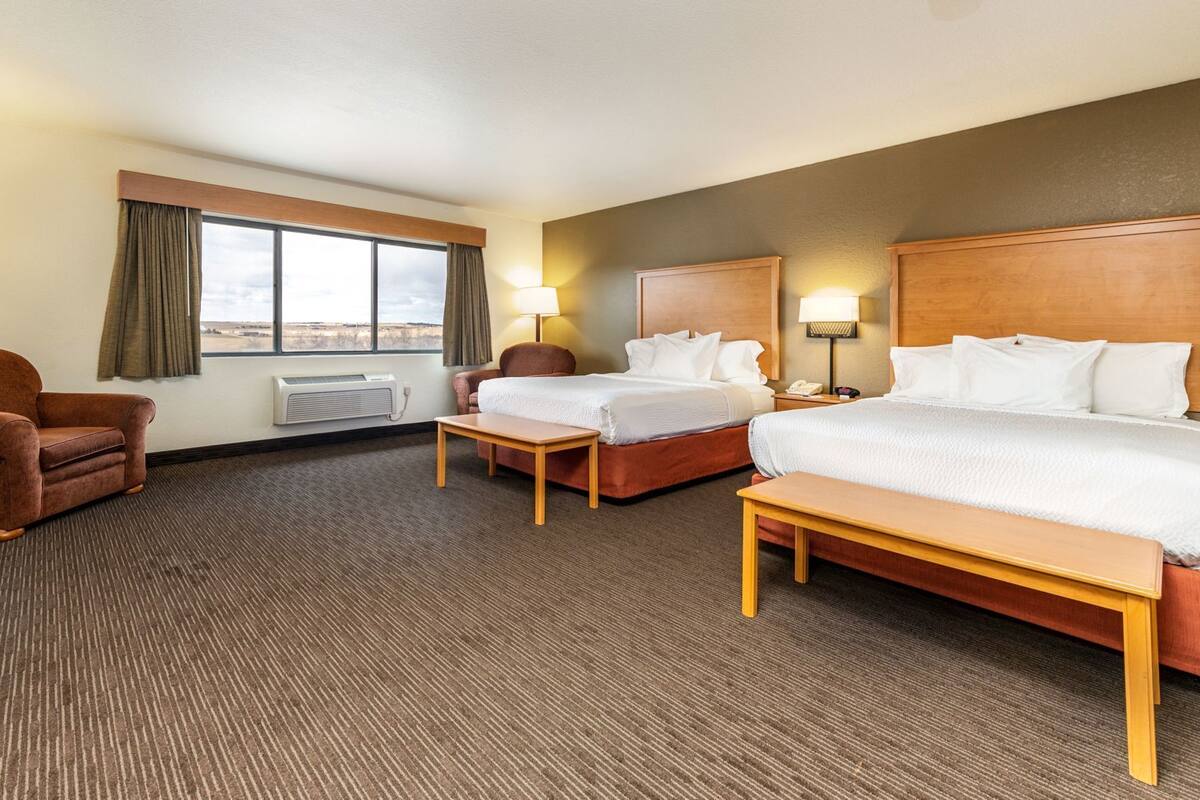 Une chambre d’hôtel avec deux lits, une chaise, une table et une fenêtre avec des rideaux.
