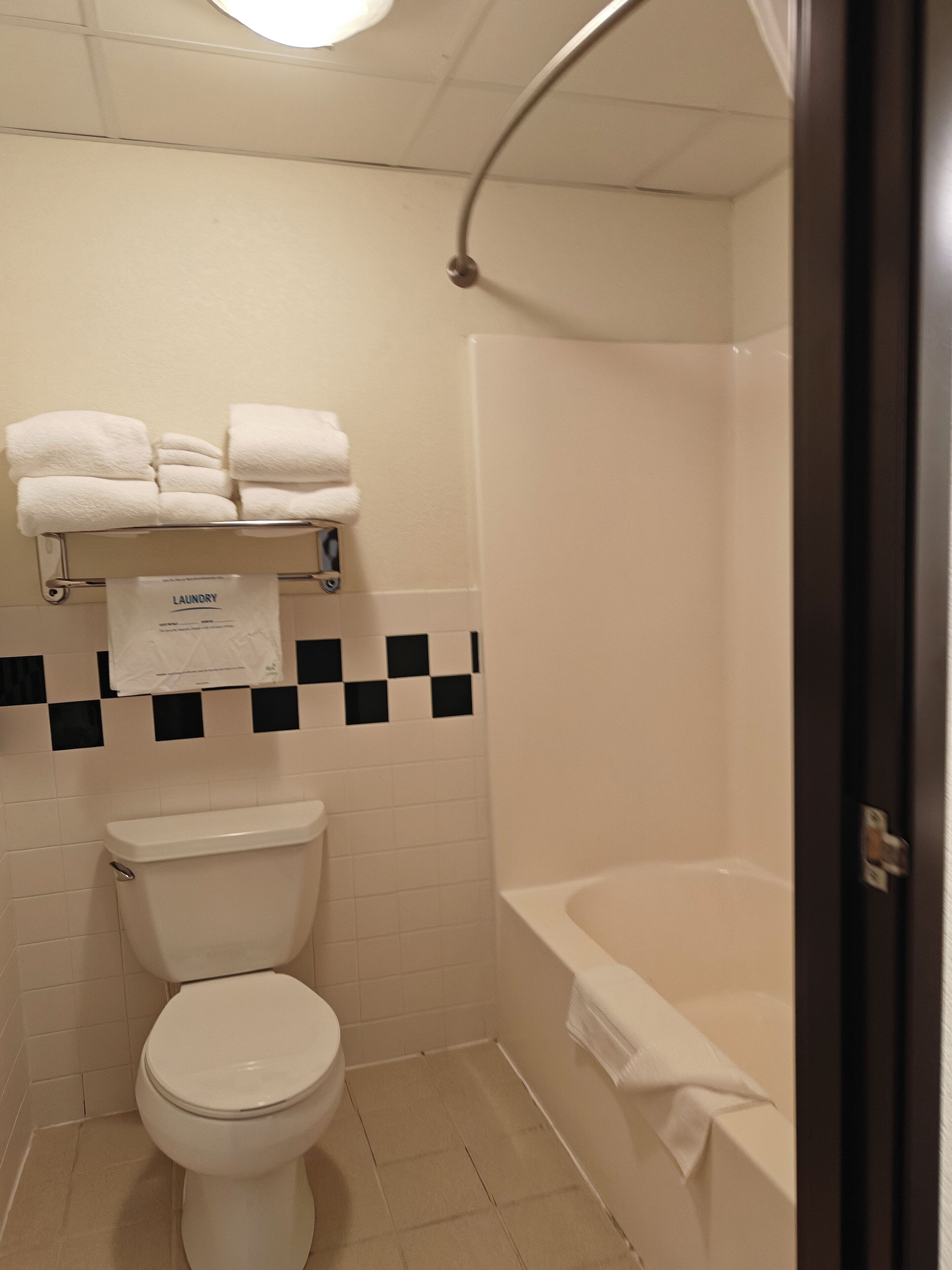 Een badkamer met toilet, een handdoekhouder met handdoeken, een douchegedeelte en een betegelde achterwand met ruitpatroon.