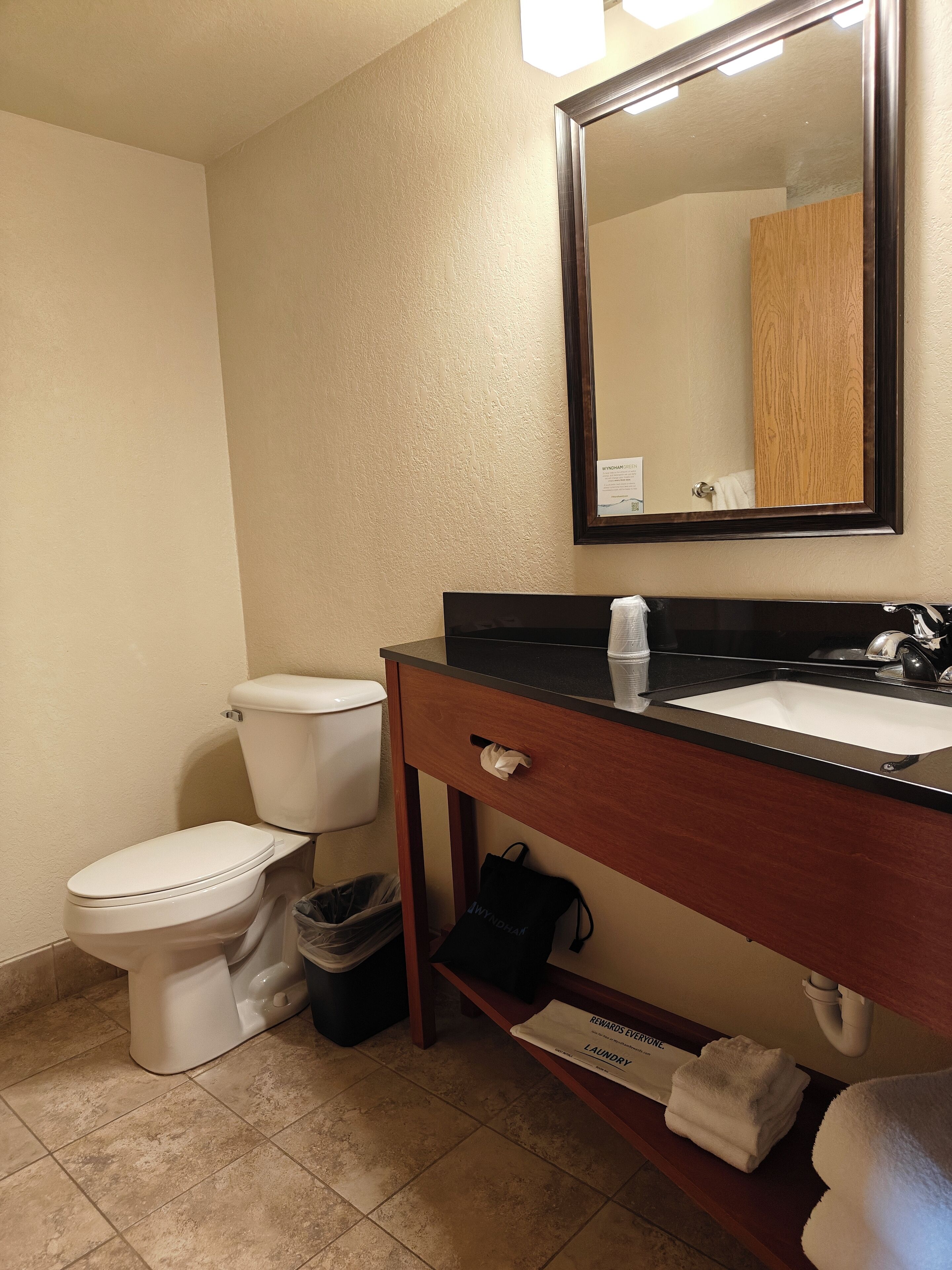 A bathroom with a toilet, sink, mirror, and a trash bin.