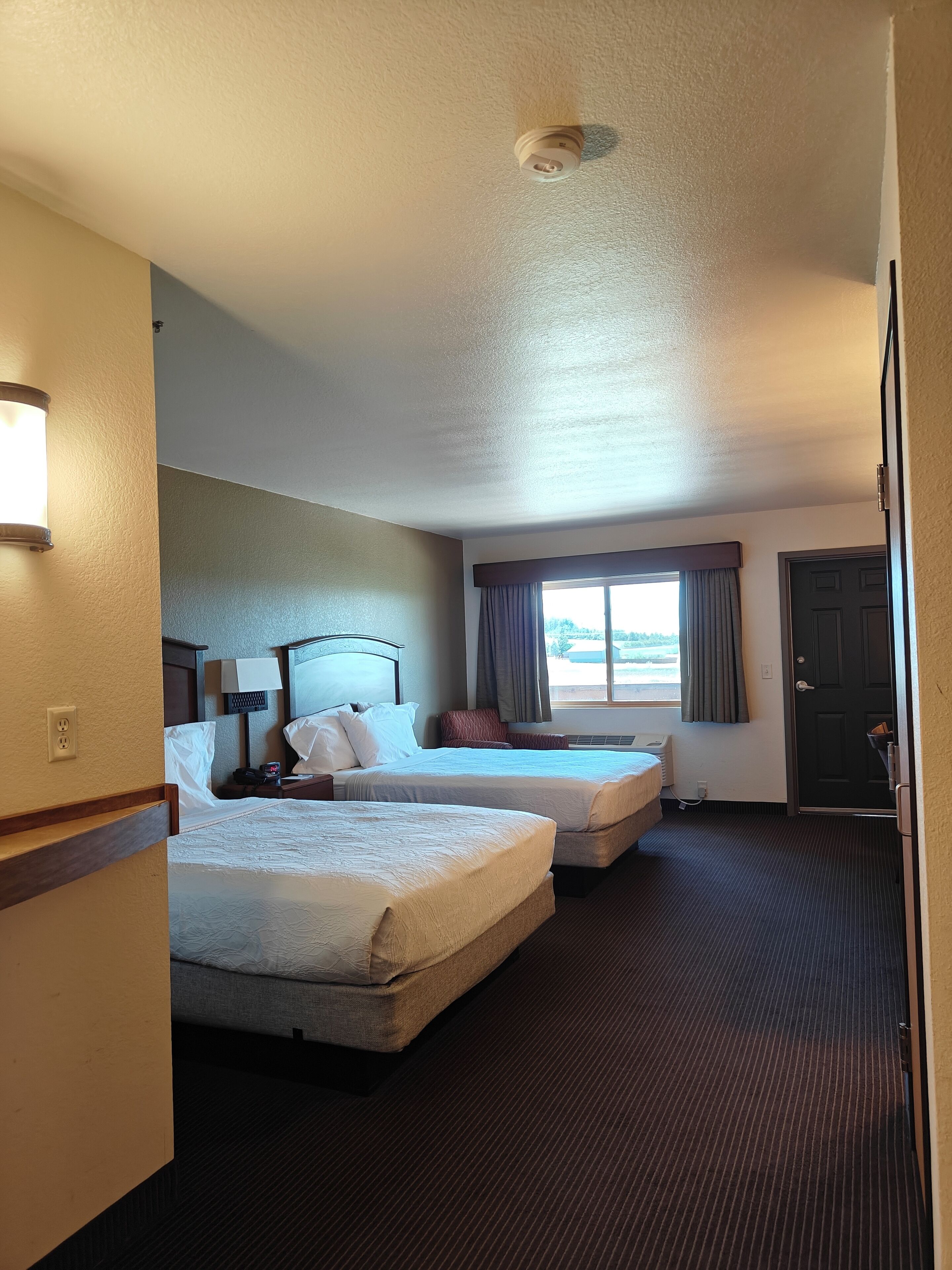 A hotel room with two beds, a window with curtains, a door, and a ceiling light.
