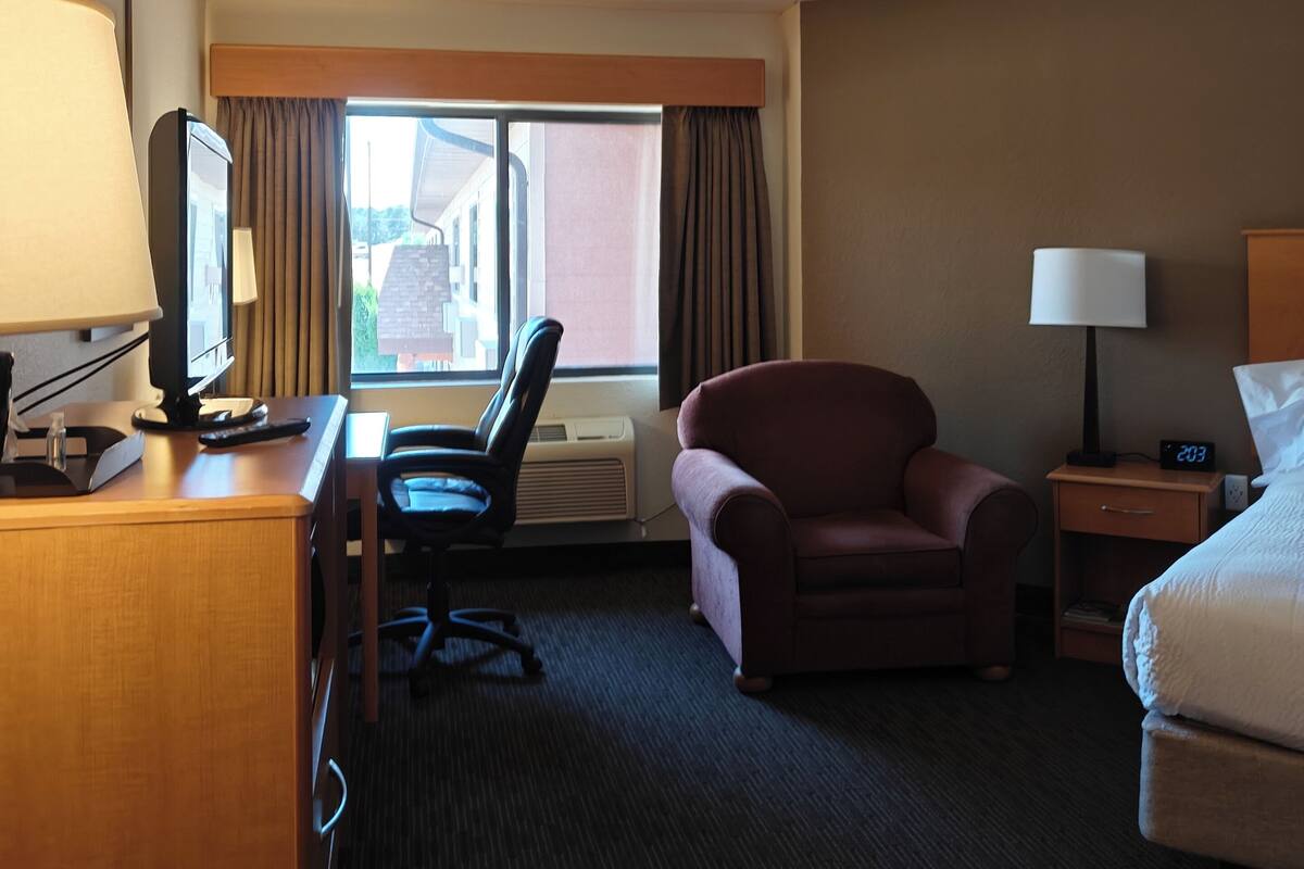 Habitación de hotel con escritorio, silla, cama y ventana con cortinas.