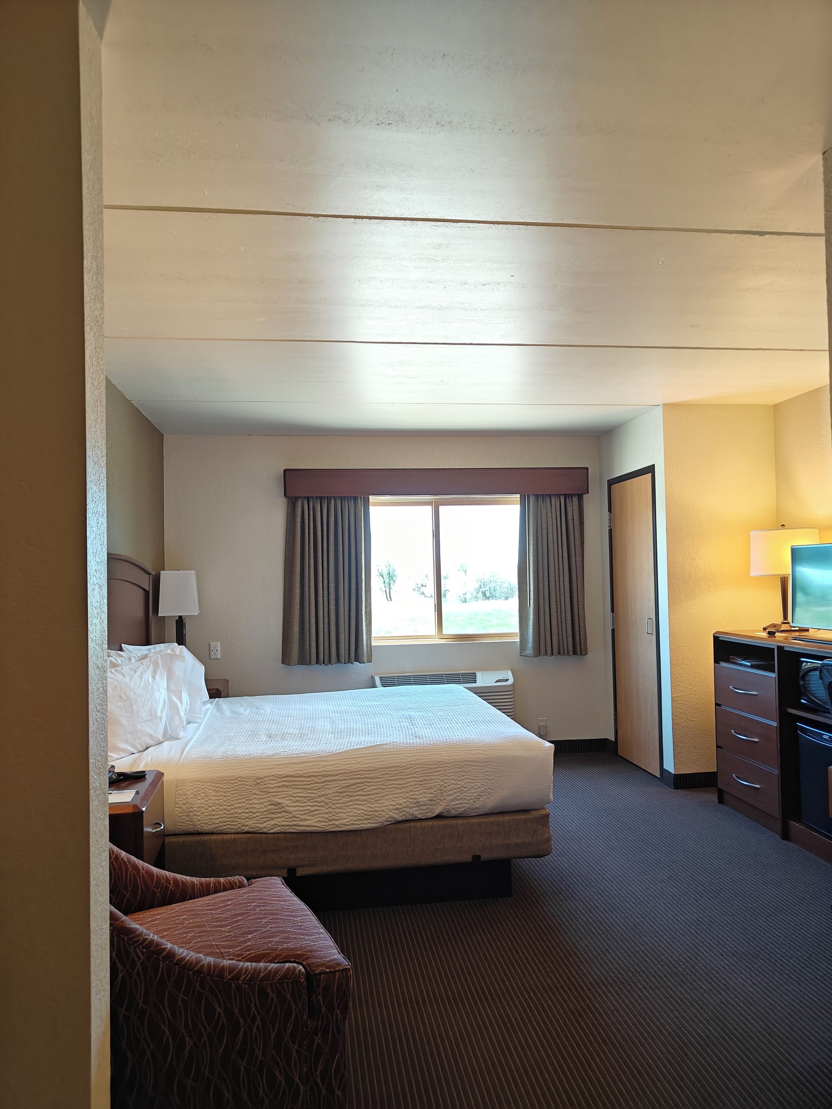 A hotel room with a bed, a desk, a chair, a television, and a window with curtains.
