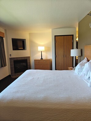 Ein Hotelzimmer mit einem großen Bett, einem Kamin, einem hölzernen Kleiderschrank, einem an der Wand montierten Fernseher und einem Nachttisch mit Lampe.