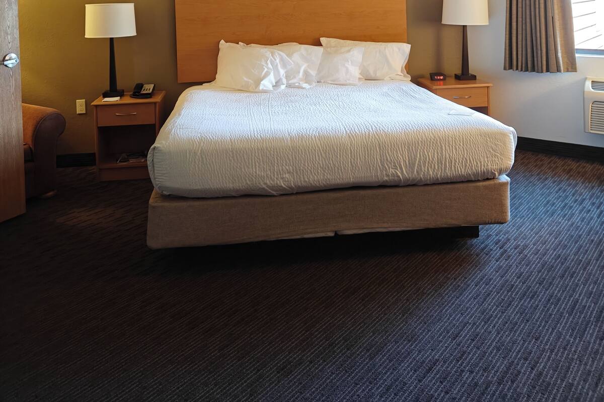 Una habitación de hotel con una cama grande, dos mesitas de noche con lámparas, un cabecero de madera, una silla y una ventana con cortinas.