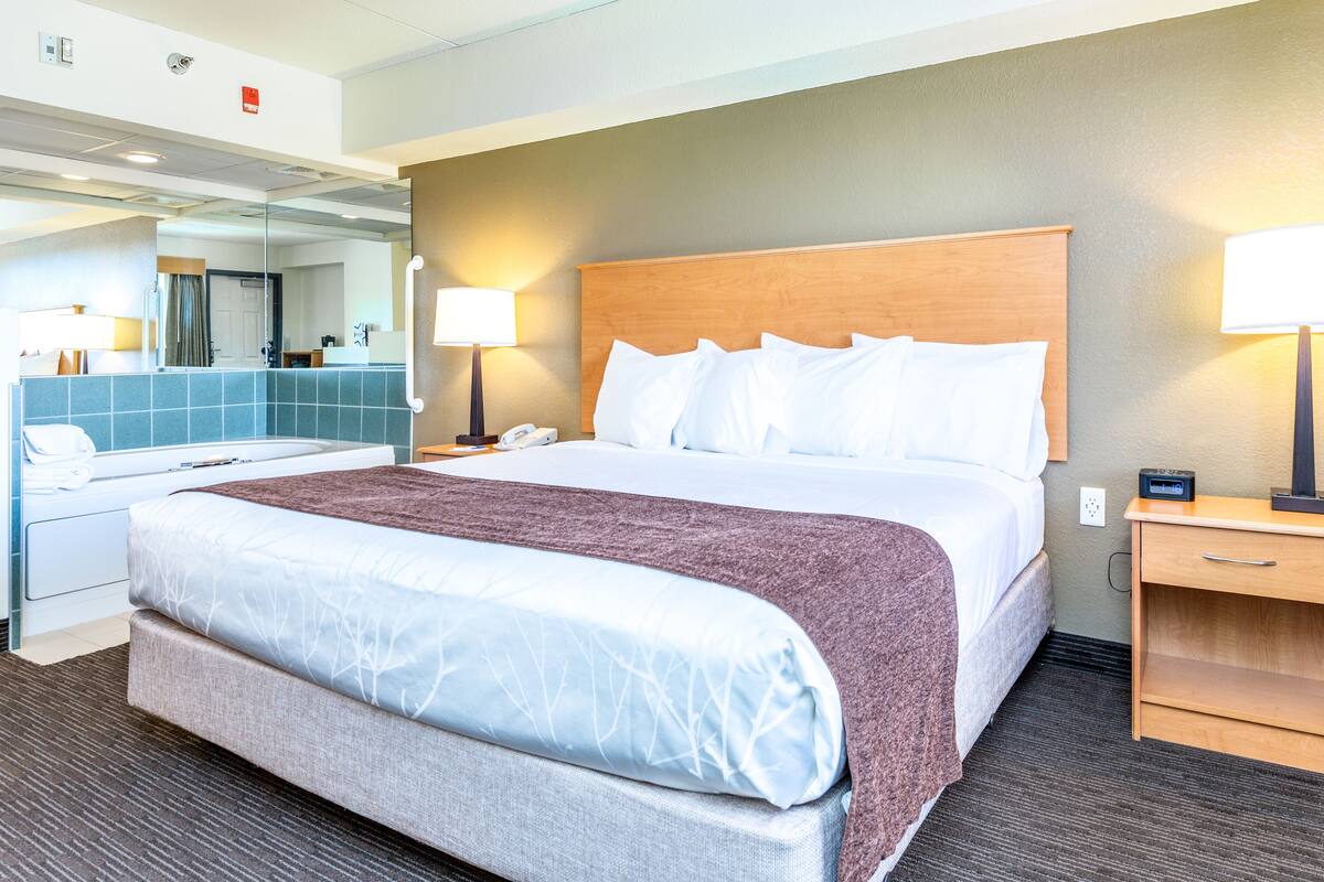 Habitación de hotel con una cama grande, dos mesitas de noche, un espejo y un baño con lavamanos y espejo.