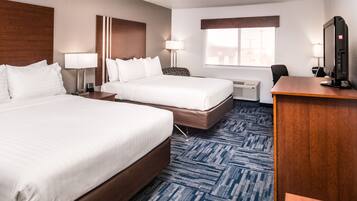 A hotel room with two beds, a desk, a computer, and a window.
