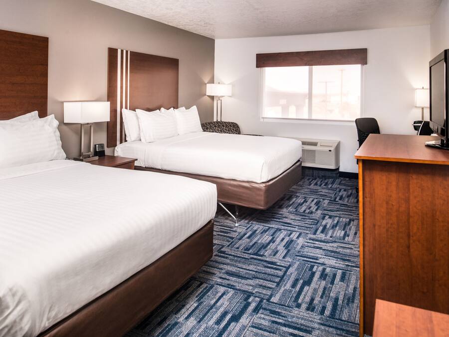 A hotel room with two beds, a desk, a computer, and a window.