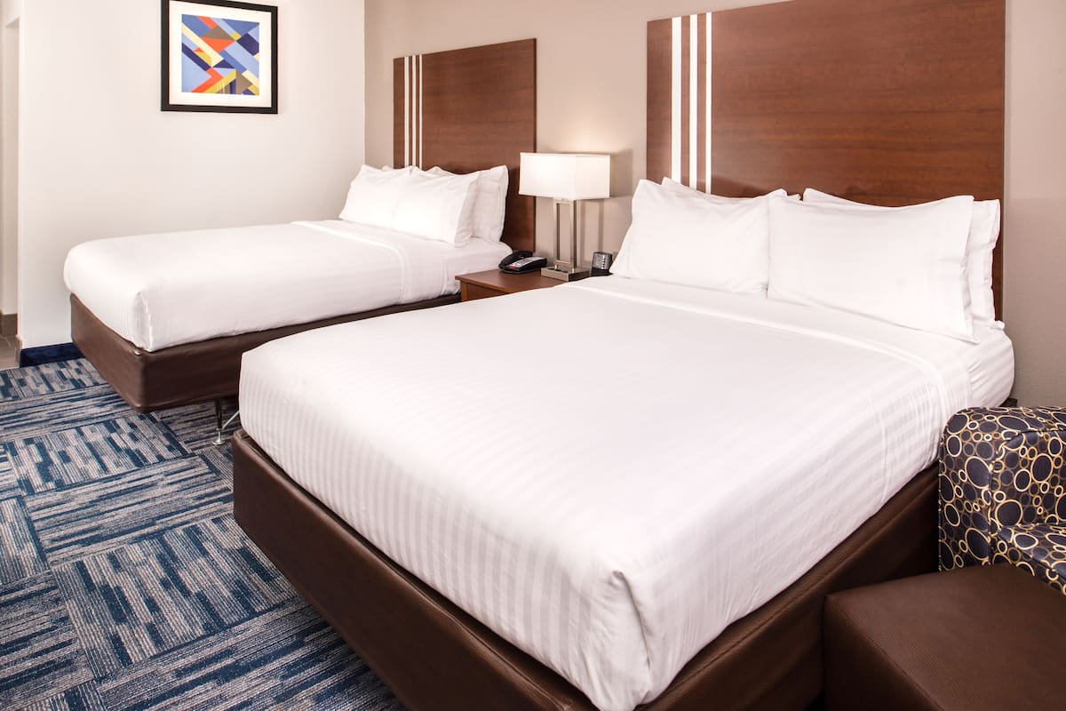 Ein Hotelzimmer mit zwei Betten, einem Holzkopfende, einem gemusterten Teppich und einem gerahmten Kunstwerk an der Wand.