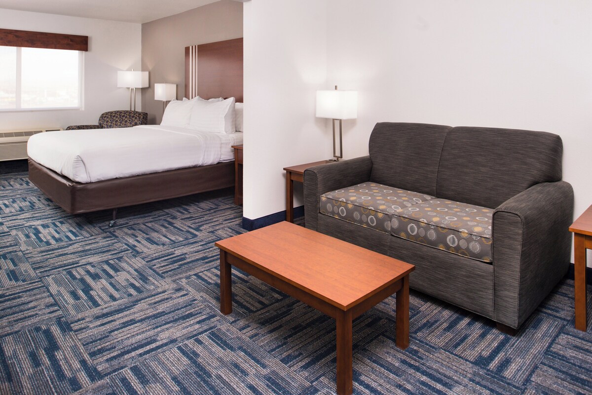 A hotel room with a bed, a sofa, a table, and a lamp.