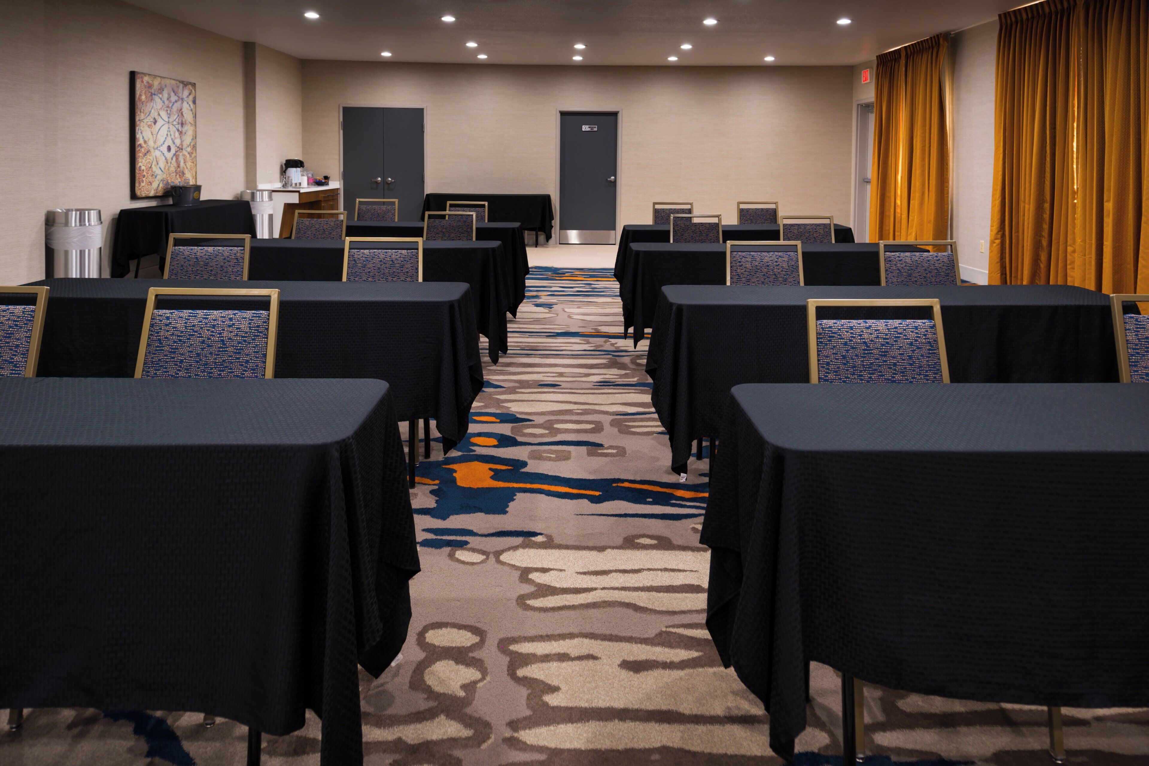 A conference room with rows of tables and chairs, a carpeted floor, and a door at the far end.
