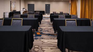 A conference room with rows of tables and chairs, a carpeted floor, and a door at the far end.