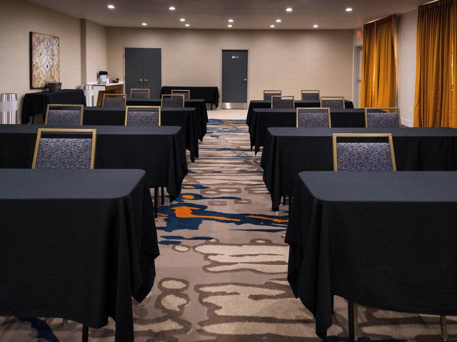 A conference room with rows of tables and chairs, a carpeted floor, and a door at the far end.