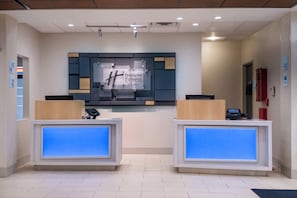 A reception desk with a digital display, a sign for Holiday Inn Express & Suites, and a fire extinguisher on the wall.