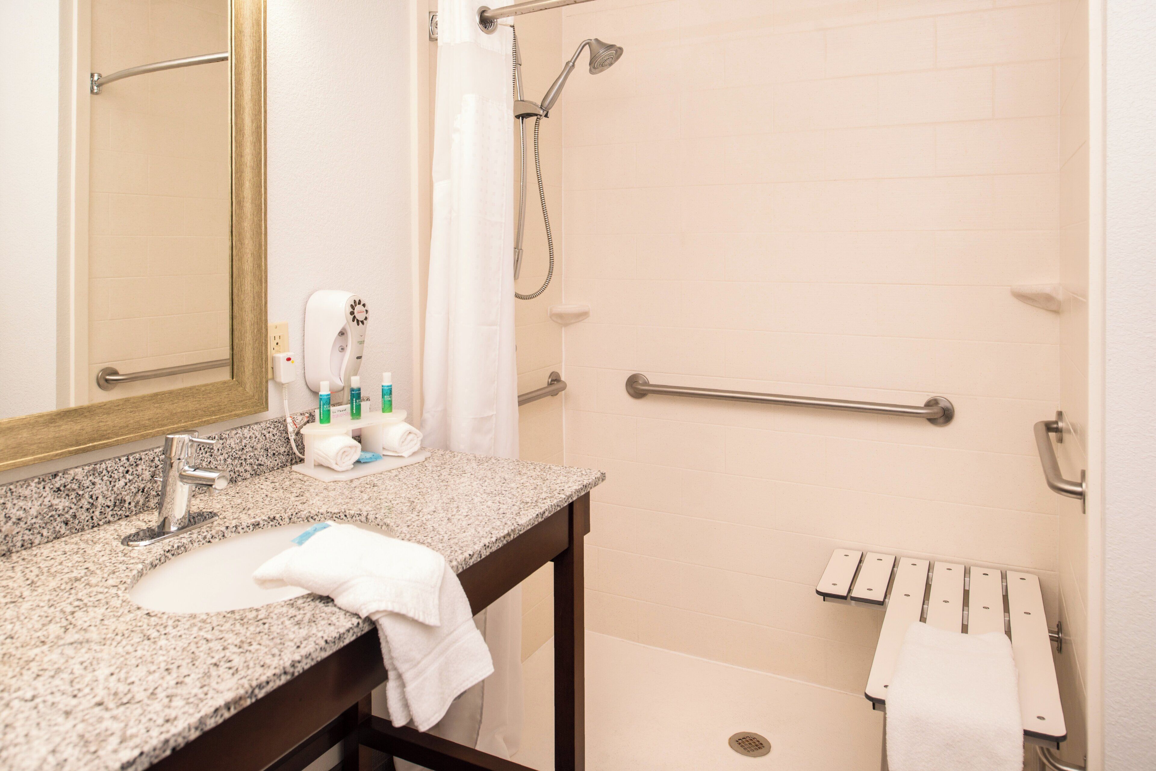 A bathroom with a granite countertop sink, a mirror, a shower with a handheld showerhead, and a grab bar.