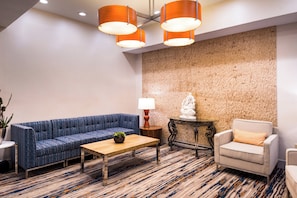 A modern lobby with a blue sofa, a wooden coffee table, a lamp, and a statue on a small table.