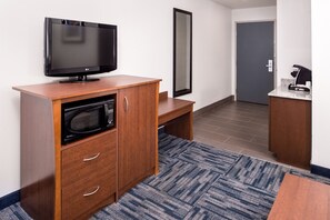 Habitación de hotel con televisor de pantalla plana, microondas, mueble de madera y una pequeña mesa.