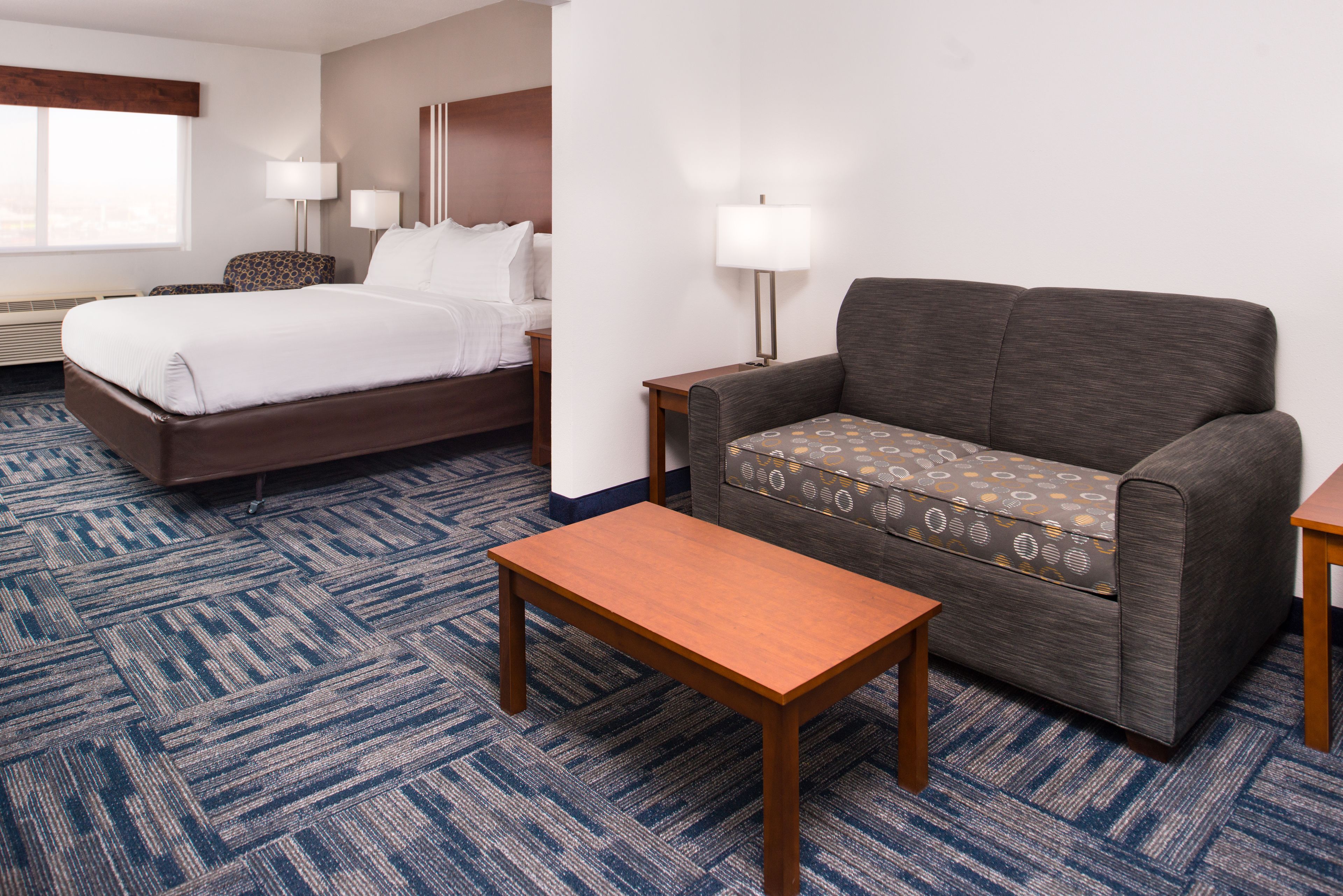A hotel room with a bed, a sofa, a small table, and two lamps.