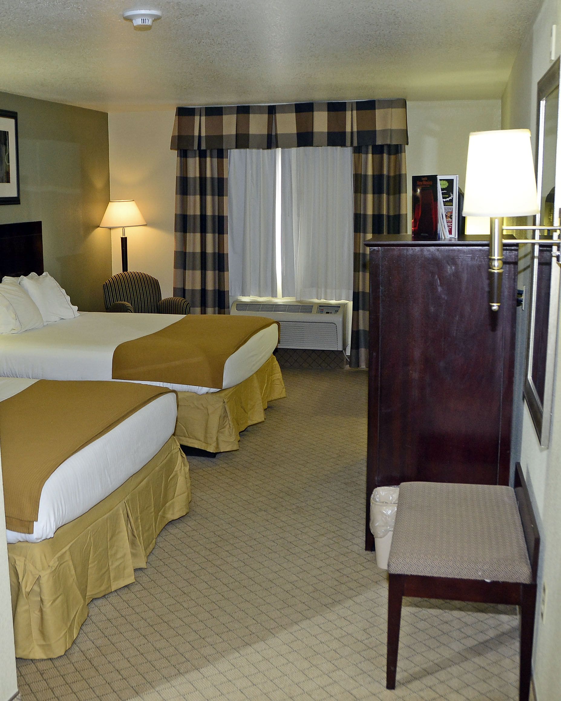 A hotel room with two beds, a desk, a chair, a lamp, and a wardrobe.