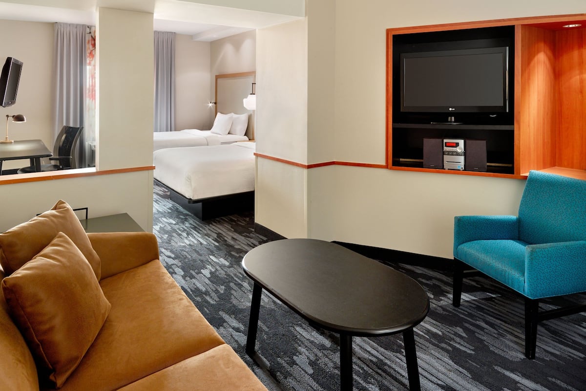 A hotel room with a bed, a TV, a sofa, a coffee table, and a TV stand with a remote control.