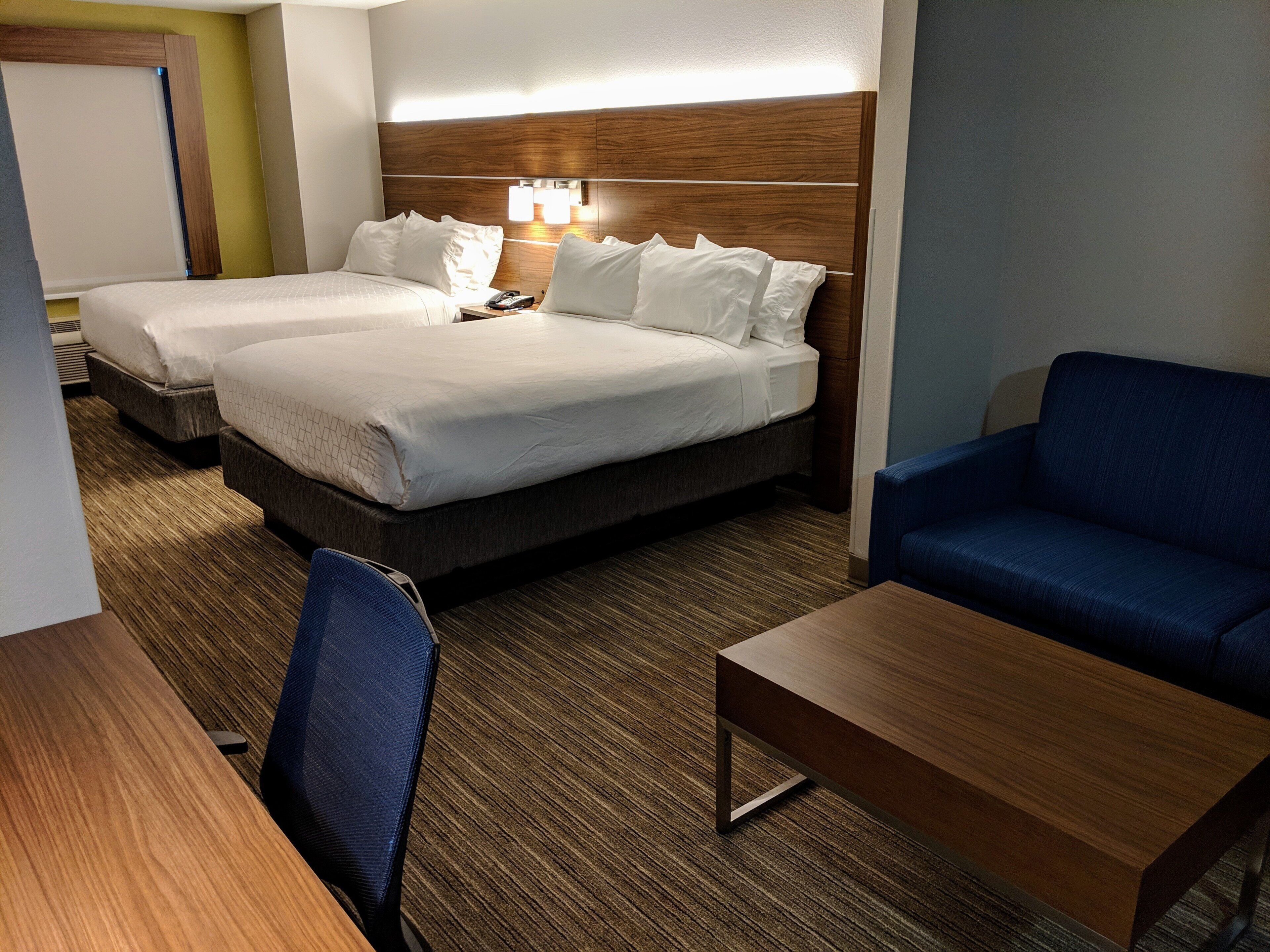 A hotel room with two beds, a desk, a chair, and a sofa.