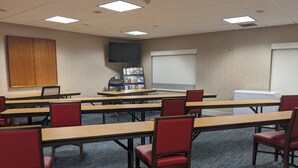 A conference room with multiple tables and chairs, a bookshelf, a whiteboard, and a television on the wall.