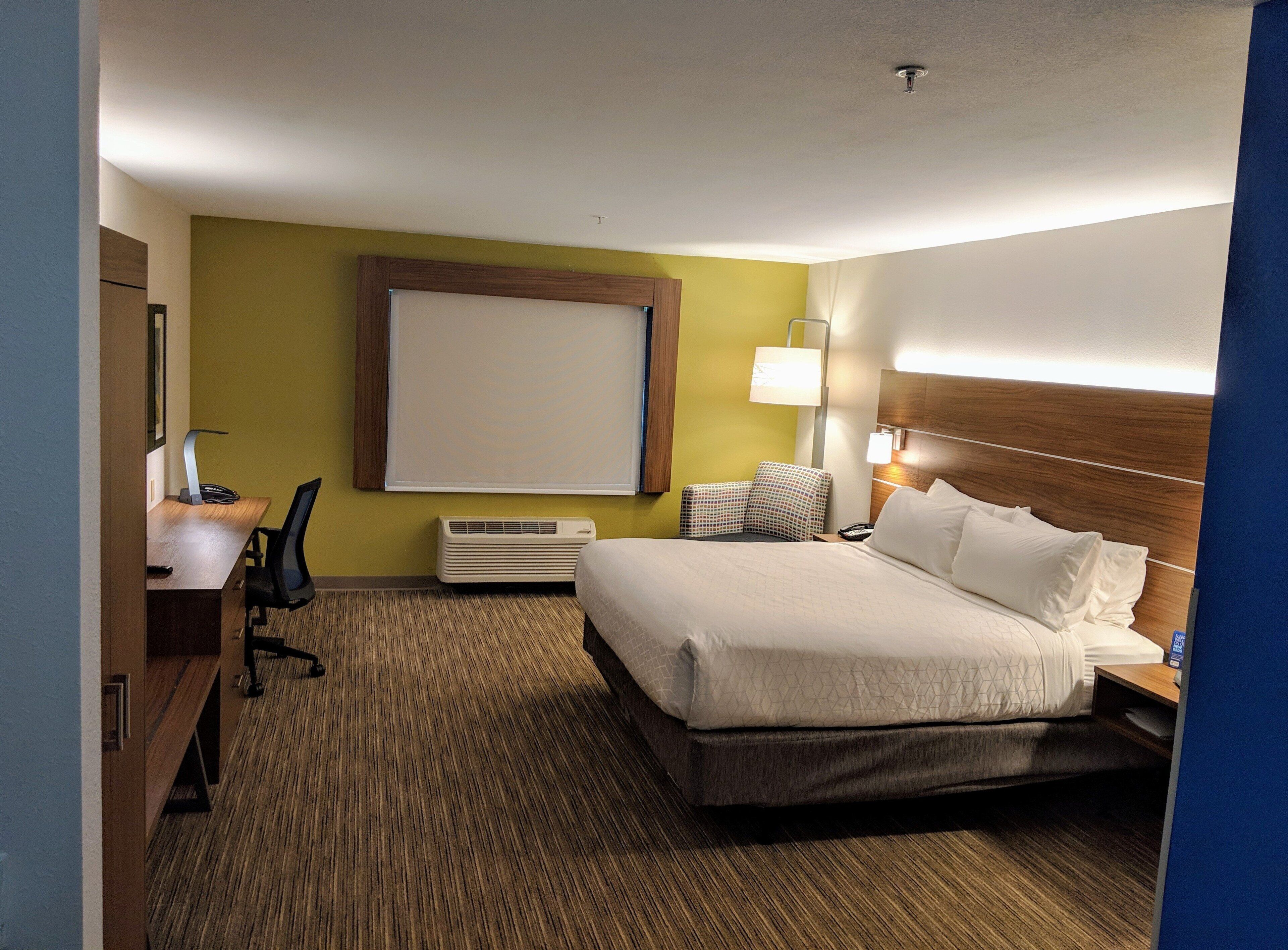 Een hotelkamer met een bed, bureau, stoel, lamp en een groot raam.