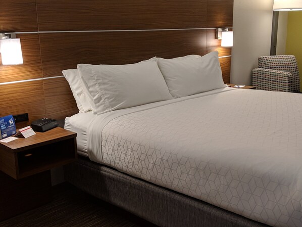A hotel room with a wooden headboard, a bed with white bedding, a nightstand with a phone and a sign, and a chair. - Holiday Inn Express & Suites Claypool Hill (Richlands Area) by IHG (Pounding Mill)