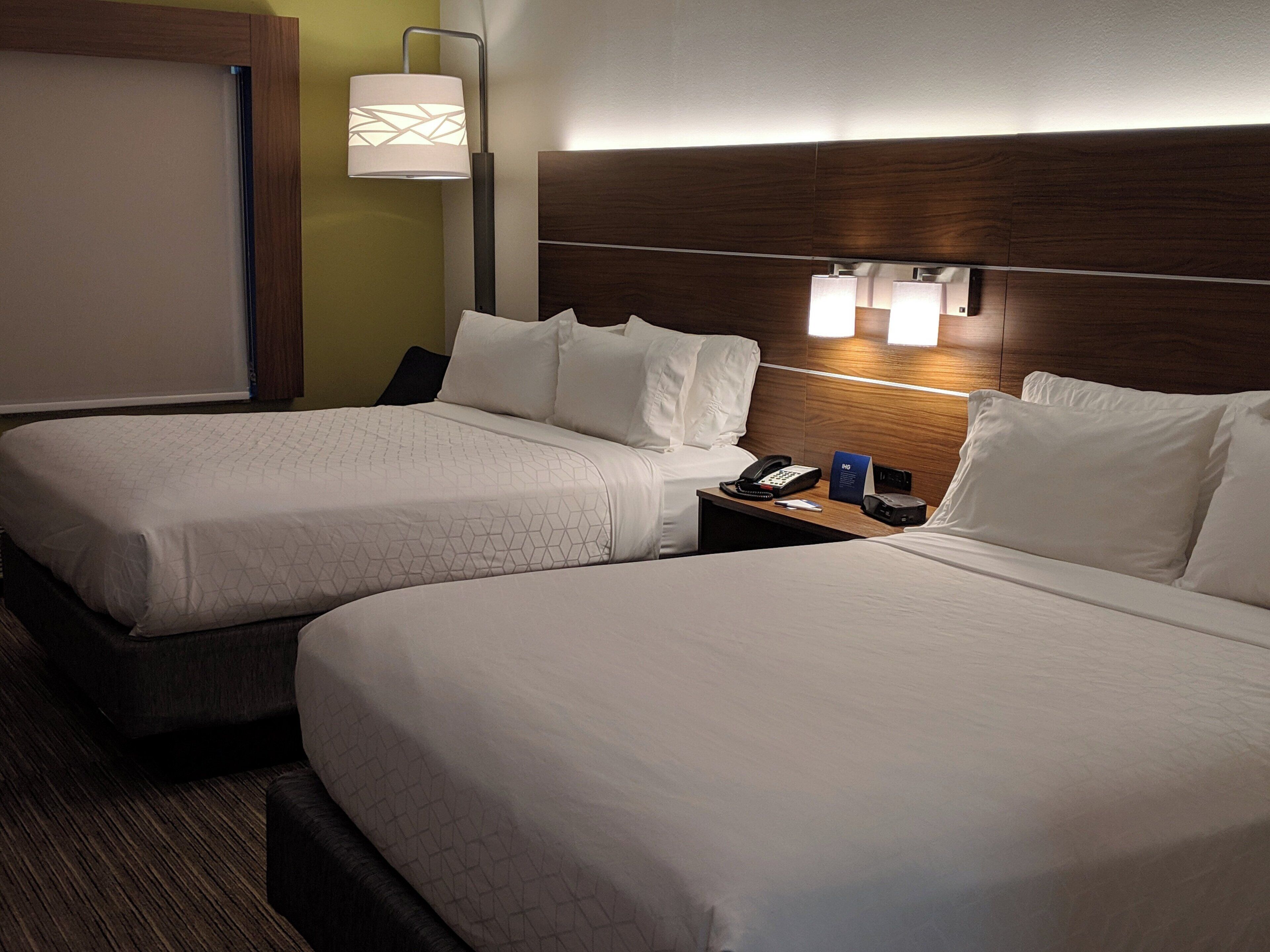 Une chambre d’hôtel avec deux lits, une table de chevet avec une lampe et un luminaire fixé au mur.