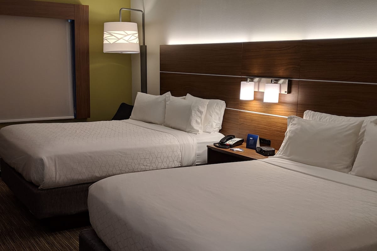 Hotellihuone, jossa on kaksi sänkyä, yöpöytä, jossa on puhelin ja lamppu, sekä seinään kiinnitetty valaisin.