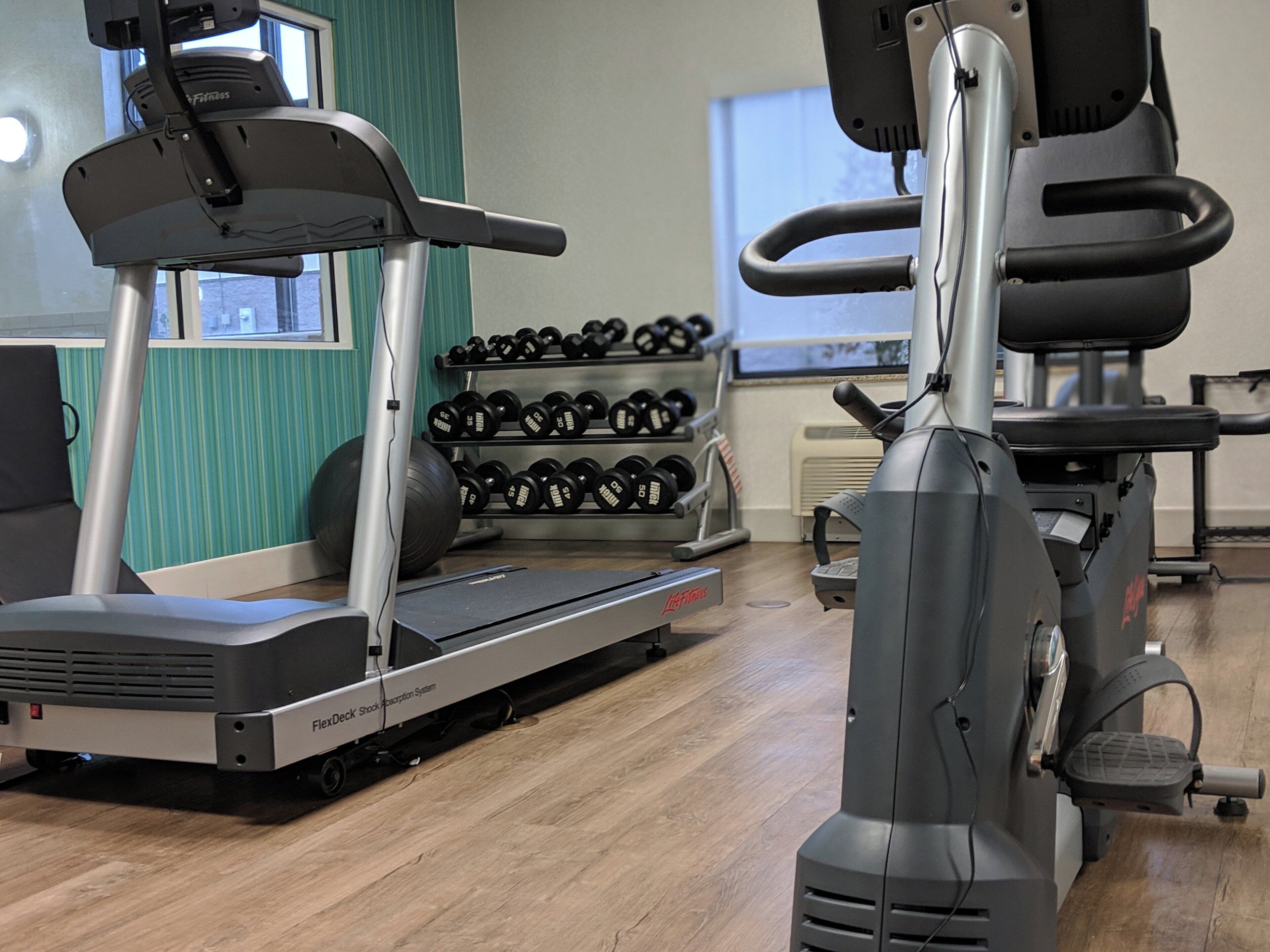 Un gimnasio con equipamiento cardiovascular, pesas y una cinta de correr.