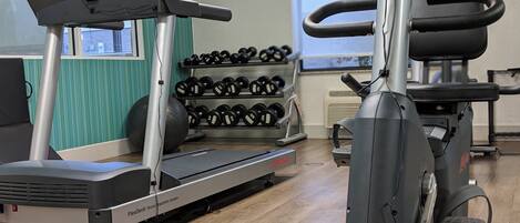 Uma academia com equipamentos de cardio, halteres e esteira.